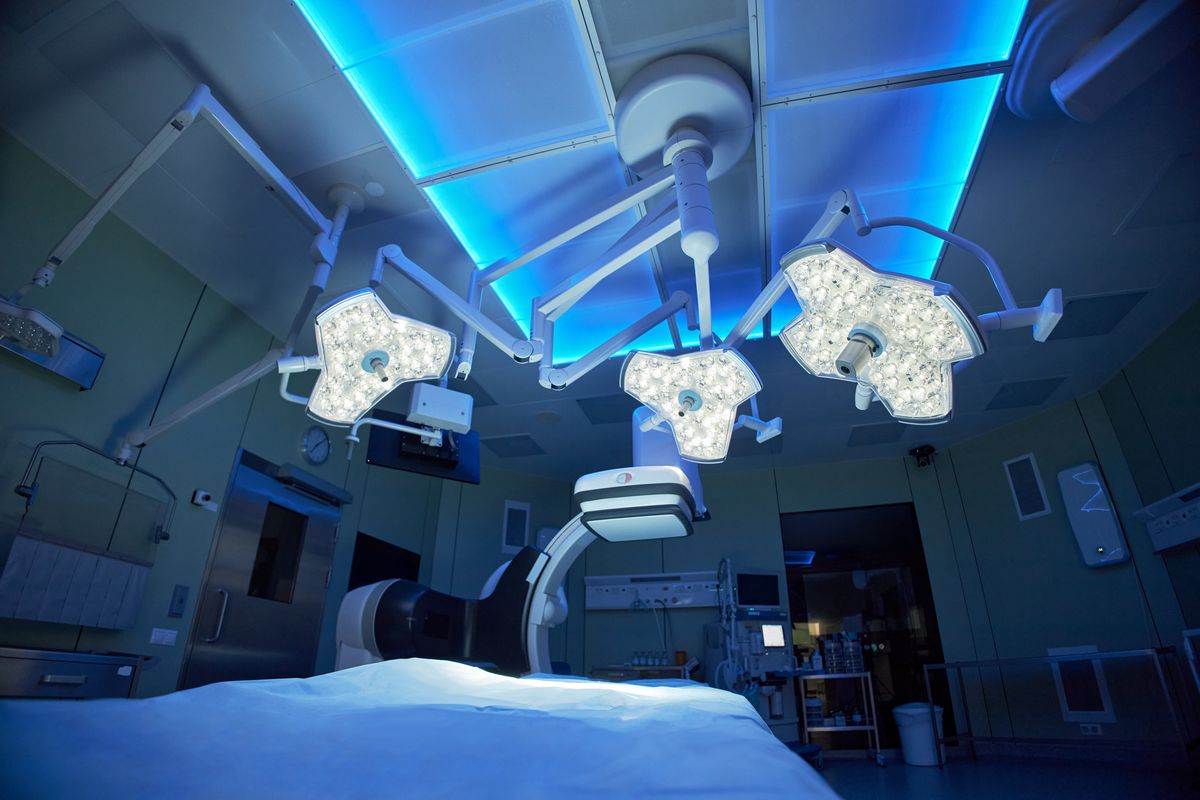 Modern operating theatre with surgical lights, a blue light ceiling and an imaging C-arm